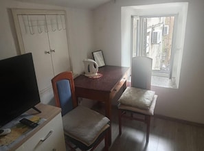 Uma pequena sala de jantar com uma mesa, cadeiras, chaleira e televisão.