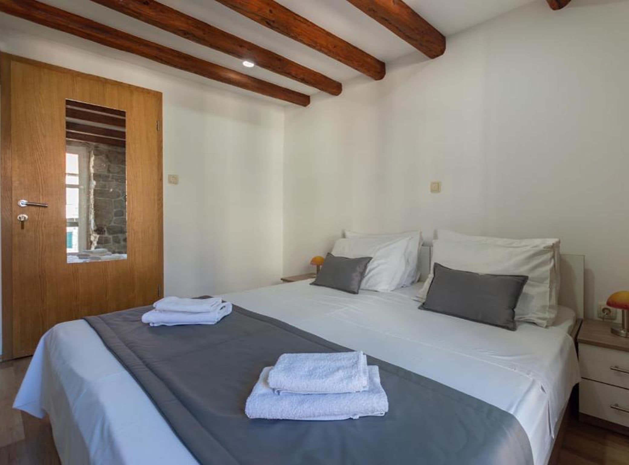 Un dormitorio con una cama, una puerta de madera y una mesita de noche con una lámpara.