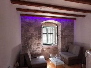 Um quarto acolhedor com parede de pedra, janela com persianas, um sofá e uma pequena mesa.