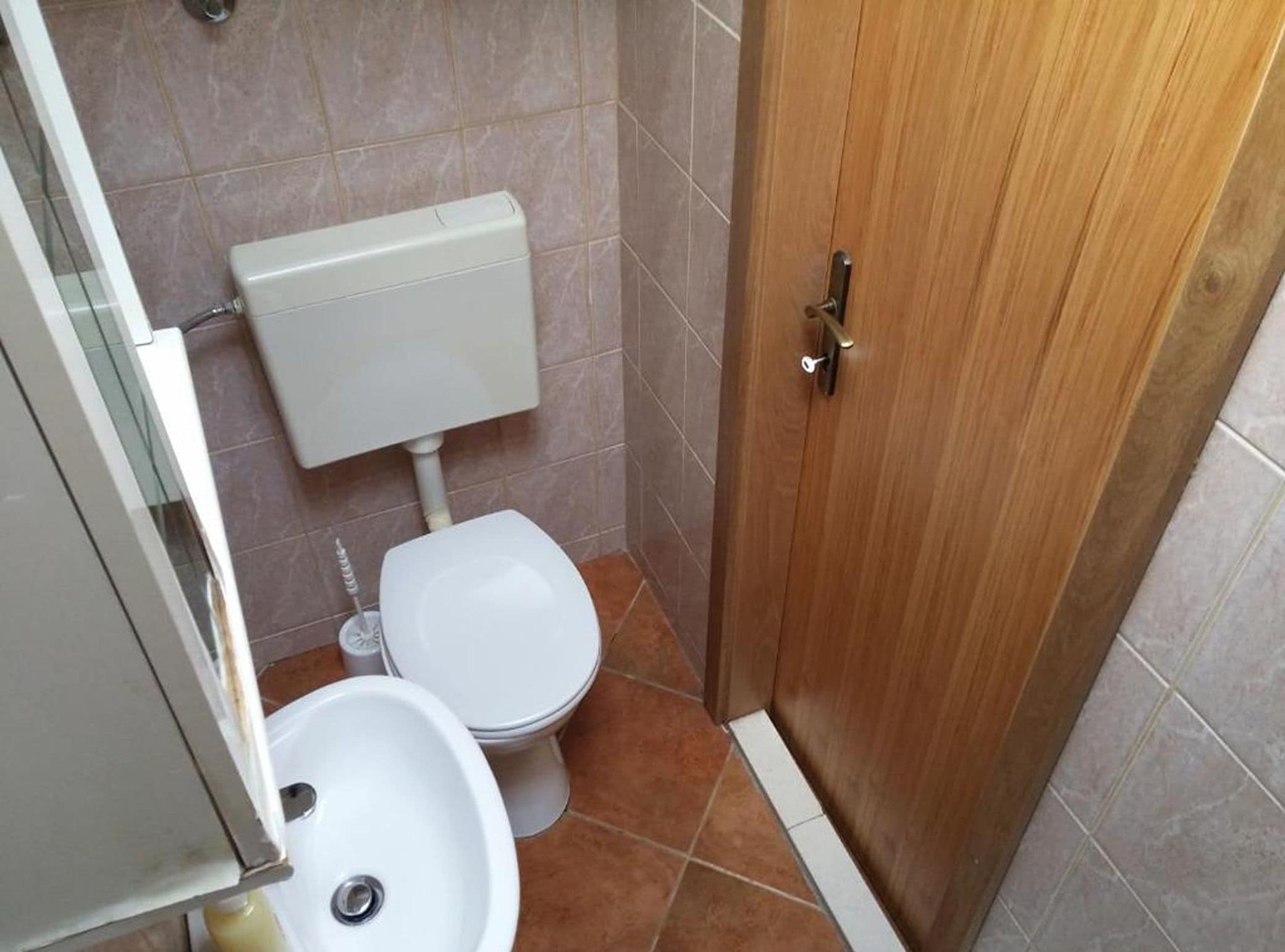 A small bathroom with a toilet, sink, and a wooden door.
