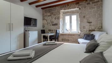 Quarto com cama, televisão, parede de pedra, janela e escrivaninha com cadeira.
