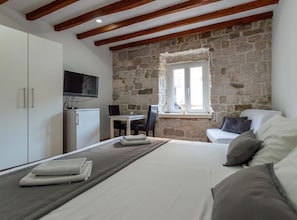 A bedroom with a bed, a TV, a stone wall, a window, and a desk with a chair. - Top Center Apartments (Split)
