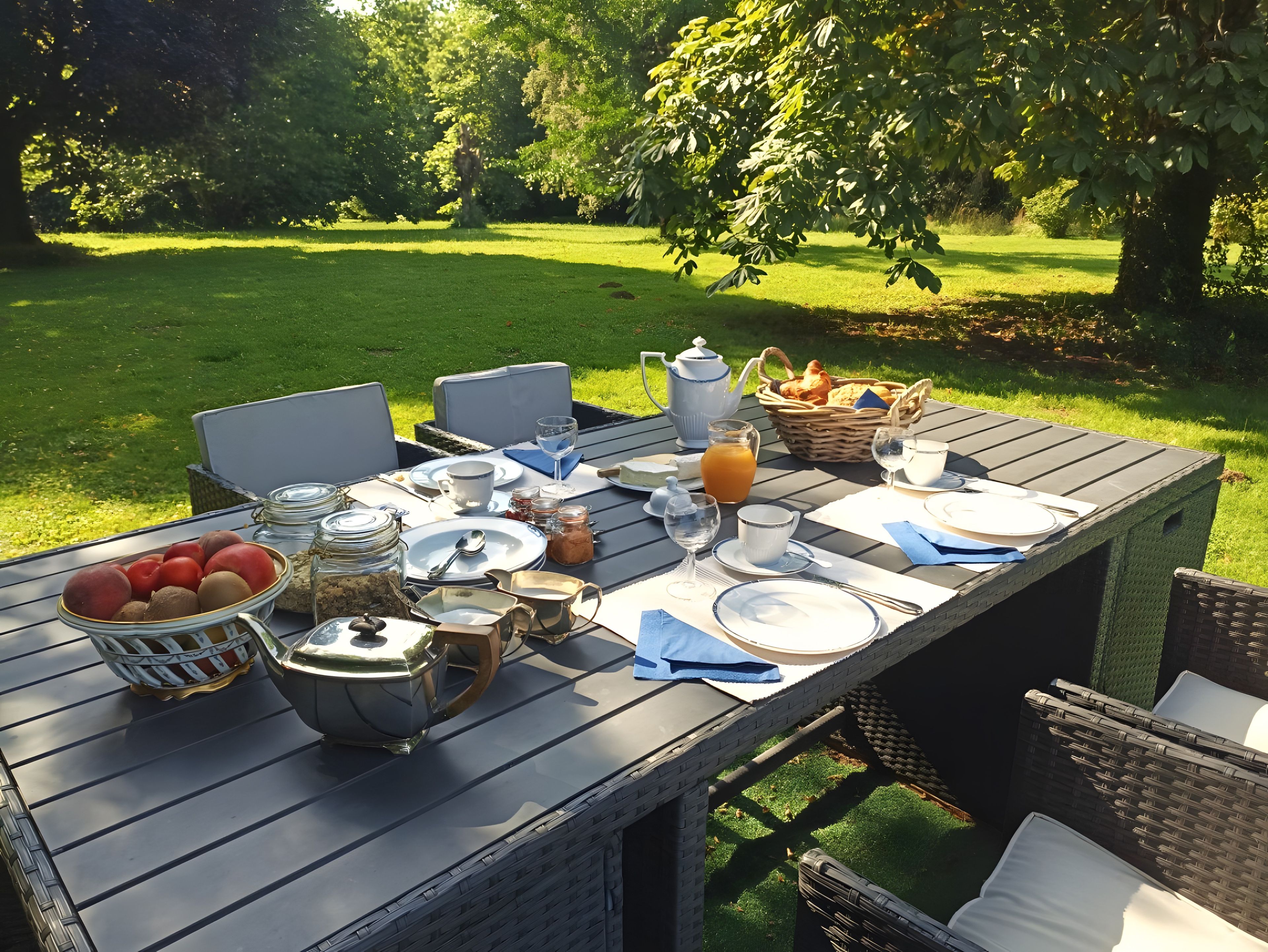 Een buitentafel gedekt met borden, bestek, glazen en een mand met brood.