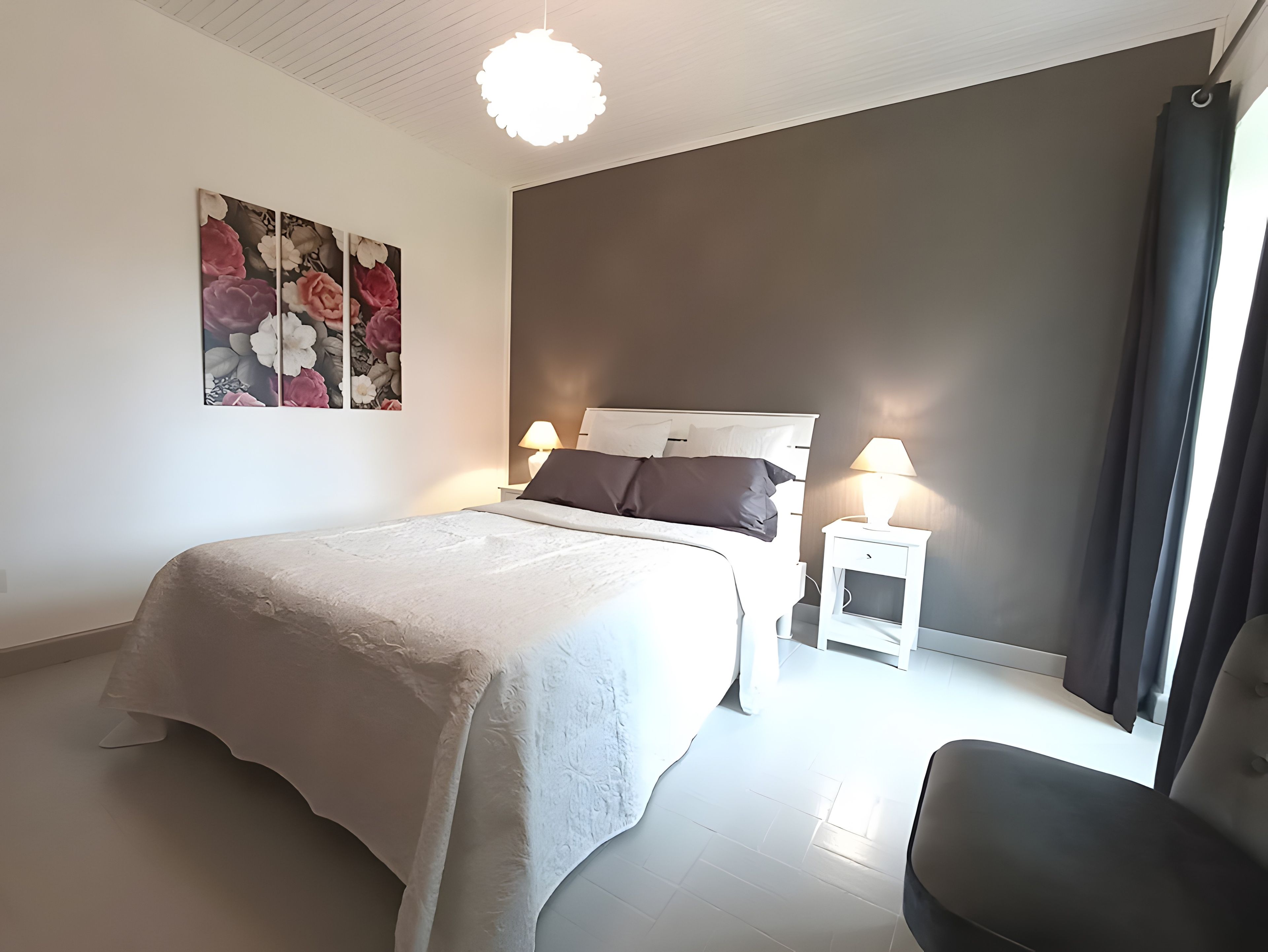 Een slaapkamer met een bed, nachtkastjes, een lamp en een schilderij aan de muur.