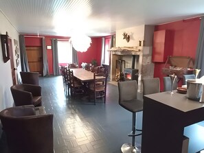Uma sala de jantar com uma longa mesa de madeira e cadeiras, uma lareira e uma área de cozinha com fogão.