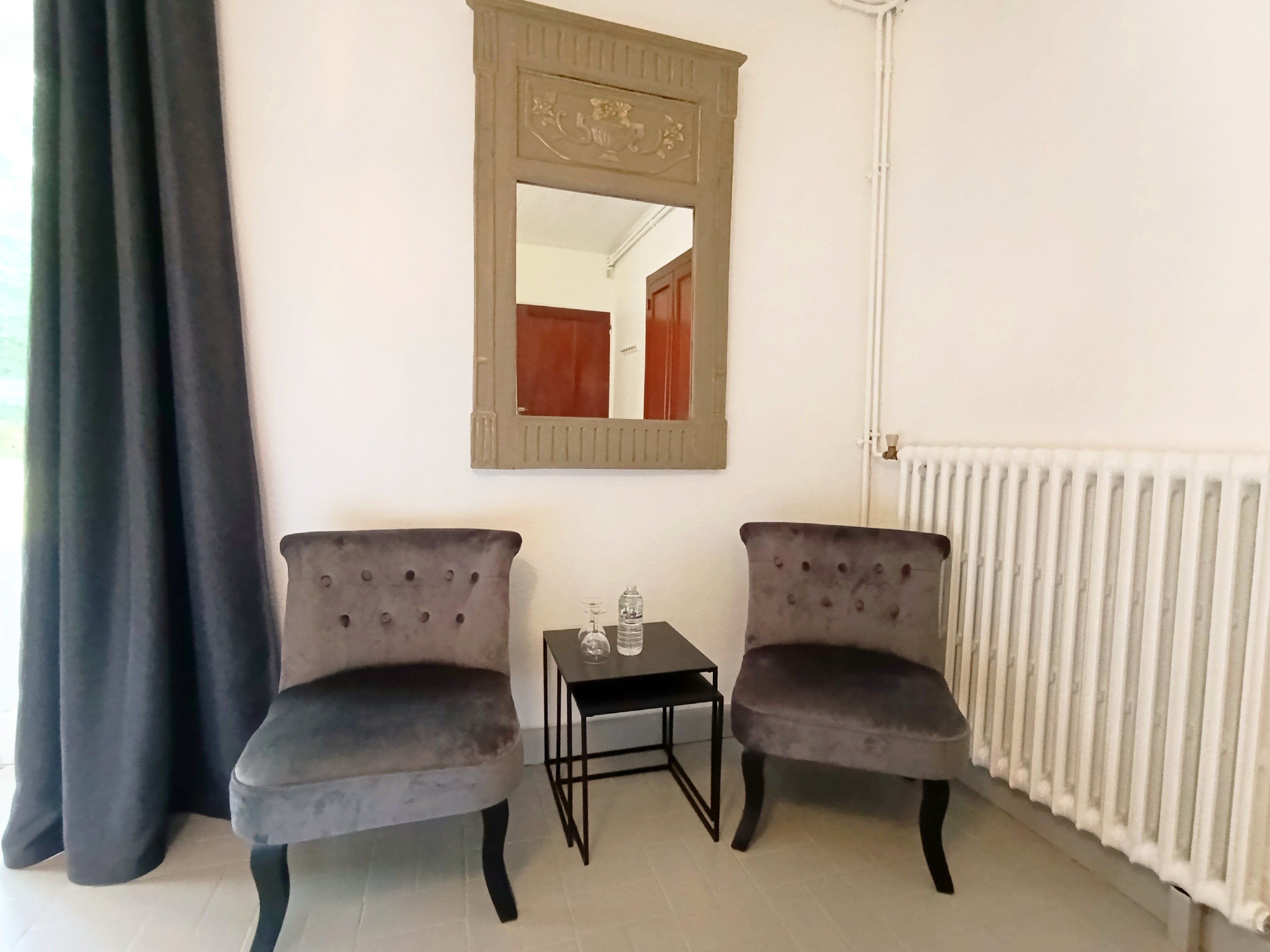 Een kamer met twee fauteuils, een tafeltje met fles en glas, een spiegel en een radiator.