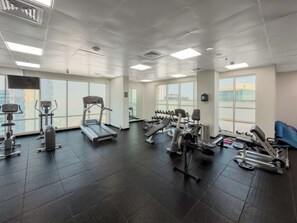 Ein Fitnessraum mit Trainingsgeräten, großen Fenstern und einem gefliesten Boden.