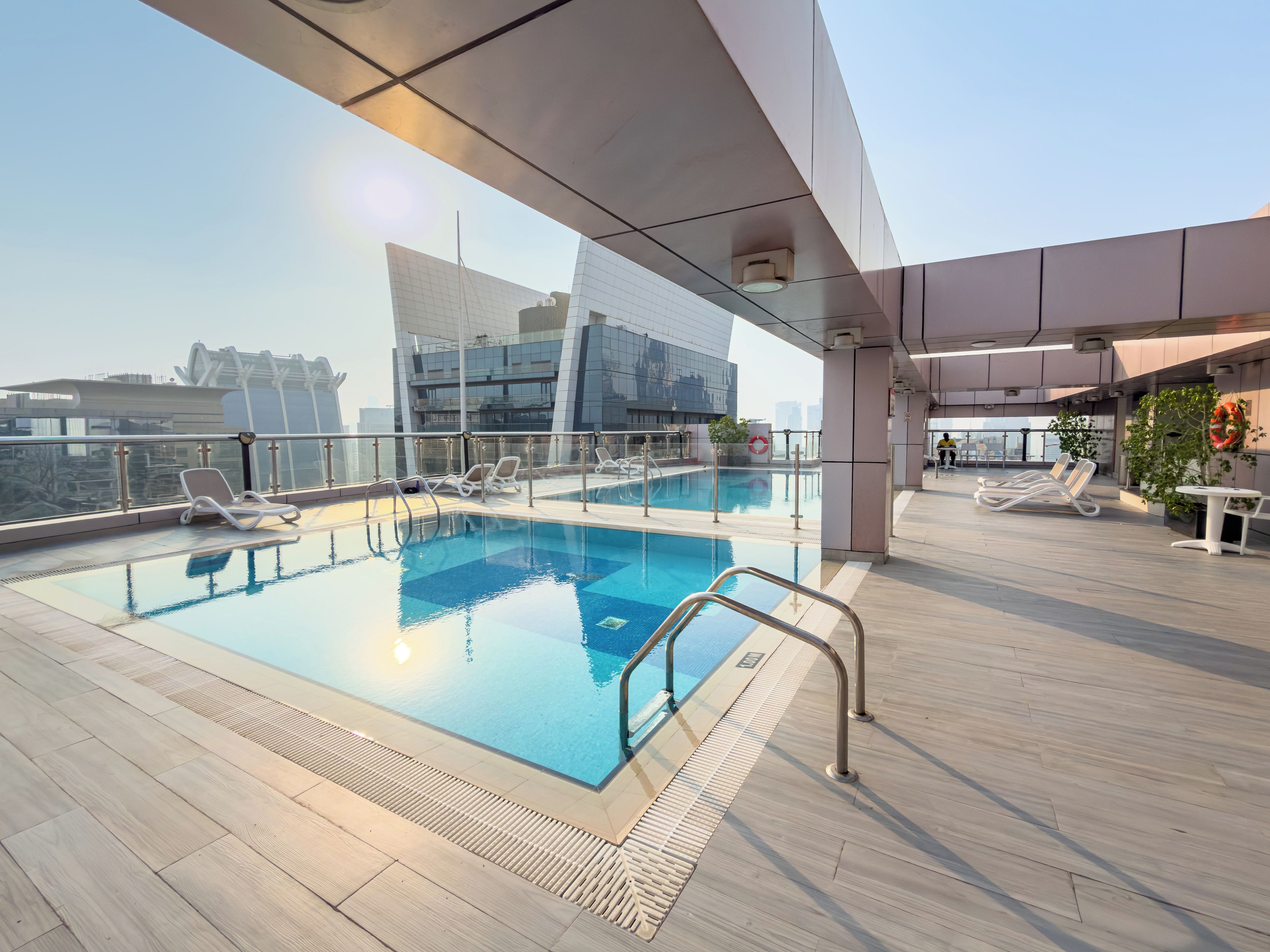 A rooftop pool with clear glass railings, sun loungers, and a view of the cityscape.