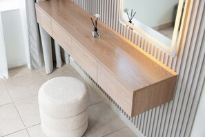 Een houten wastafelmeubel met een spiegel, een klein krukje en een decoratief object op het aanrecht.