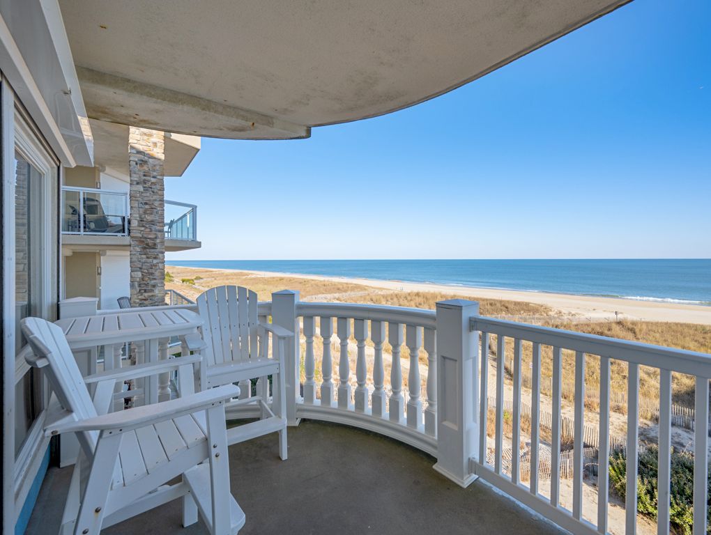 En balkon med hvide Adirondack-stole og gelænder, der vender ud mod en strand.