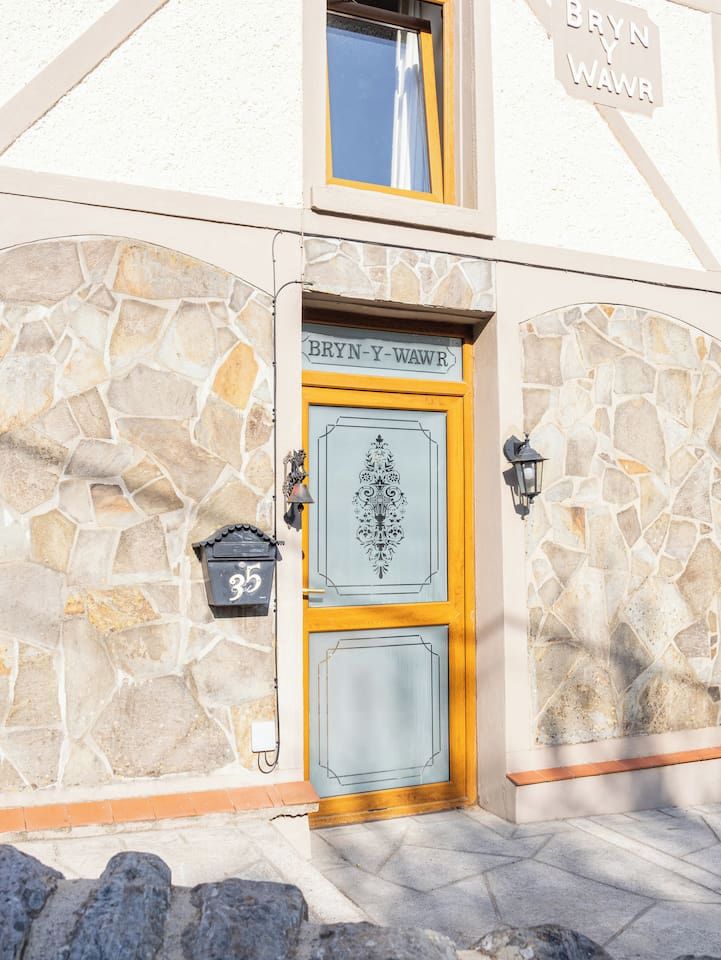 Eine steinerne Fassade mit einer gelb gerahmten Tür mit der Aufschrift 'BRYN Y WAWR' und einem Briefkasten mit der Nummer 35.