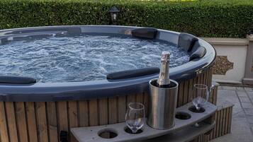 A hot tub with a wooden exterior, a metal container with a bottle, and two glasses.