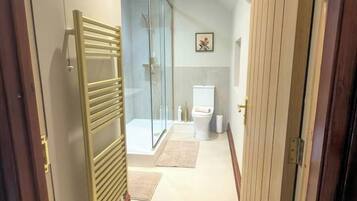 En gang der fører til et badeværelse med et glasbadeværelsesafskærmning, et toilet og en bøjle til håndklæder.