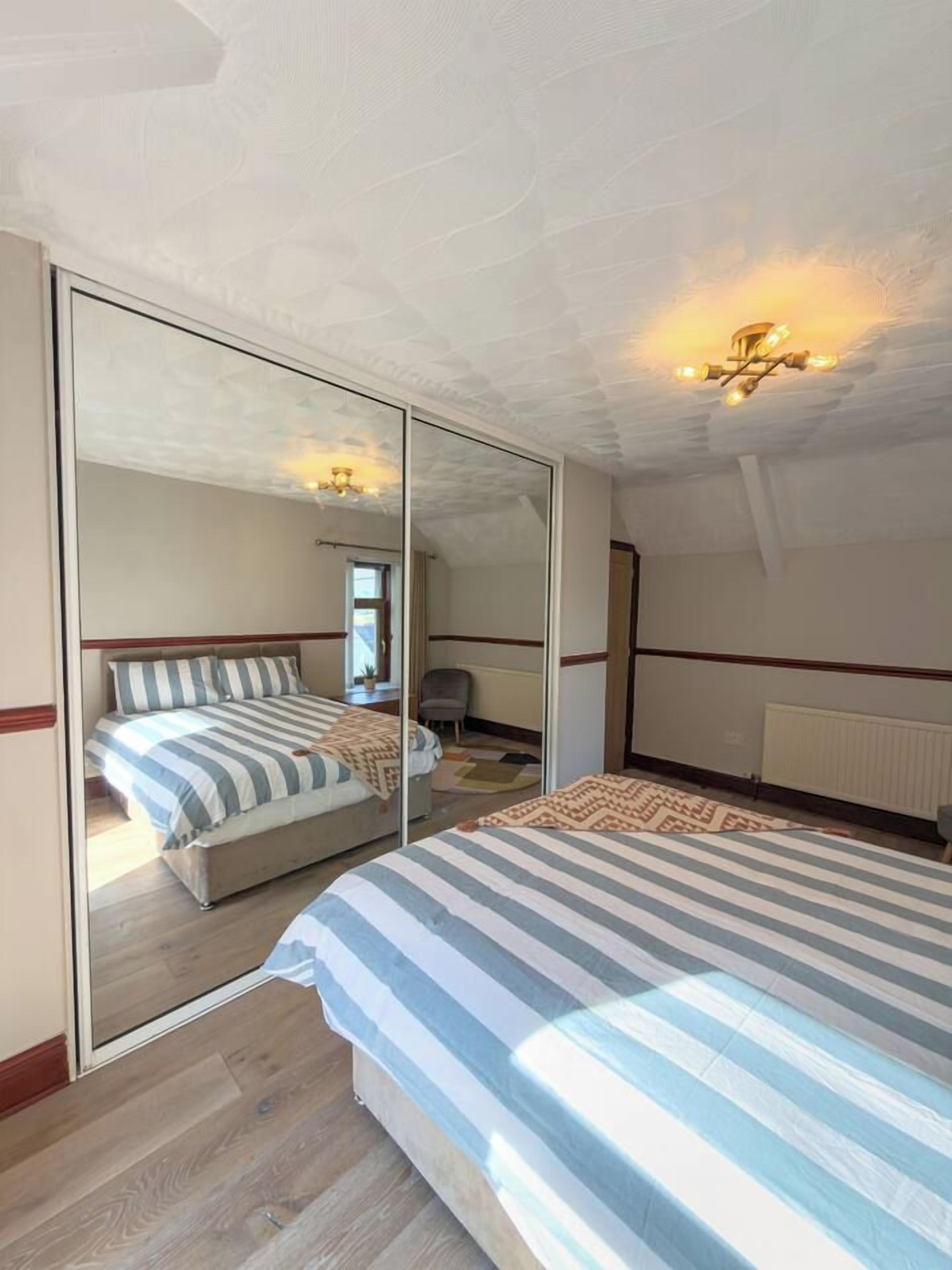 Ein Schlafzimmer mit einem großen Spiegel, einem Bett mit gestreifter Bettwäsche, einem Sessel und einer Deckenleuchte.