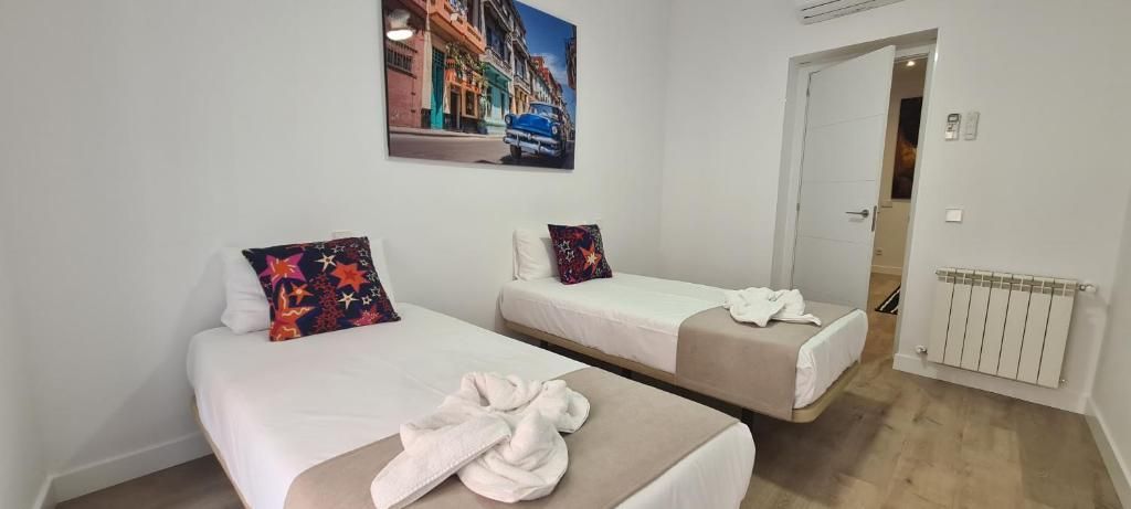 A hotel room with two single beds, a white wall, a radiator, and a door leading to another room.