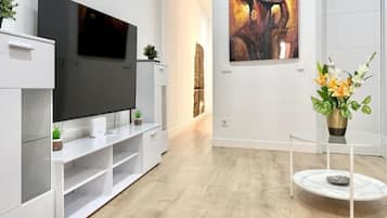 Una sala moderna con un televisor de pantalla plana, un mueble blanco para entretenimiento y una mesa de centro de vidrio.