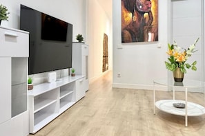 Una sala moderna con un televisor de pantalla plana, un mueble blanco para entretenimiento y una mesa de centro de vidrio.