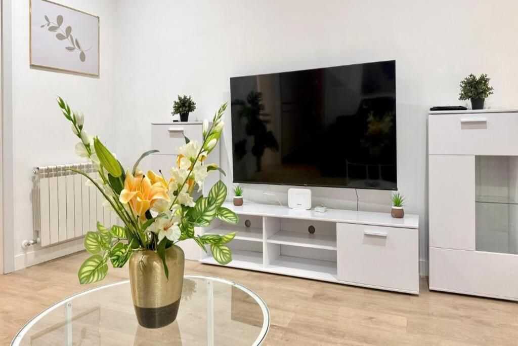 A modern living room with a flat-screen TV, white cabinetry, and a glass coffee table with a floral arrangement.