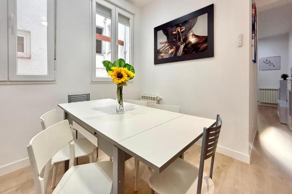A dining area with a white table and chairs, a vase with a sunflower, and a framed picture on the wall.