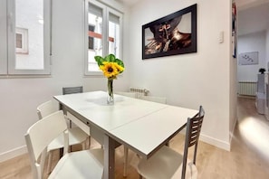 Un comedor con una mesa y sillas blancas, un jarrón con un girasol y un cuadro en la pared.