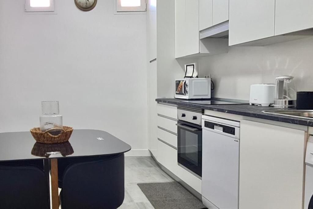 A compact kitchen with a microwave, toaster, and coffee maker on the countertop, a dishwasher, and a small table with a basket.