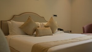 A hotel room with a bed, pillows, a bedside table with a phone, and a chair.