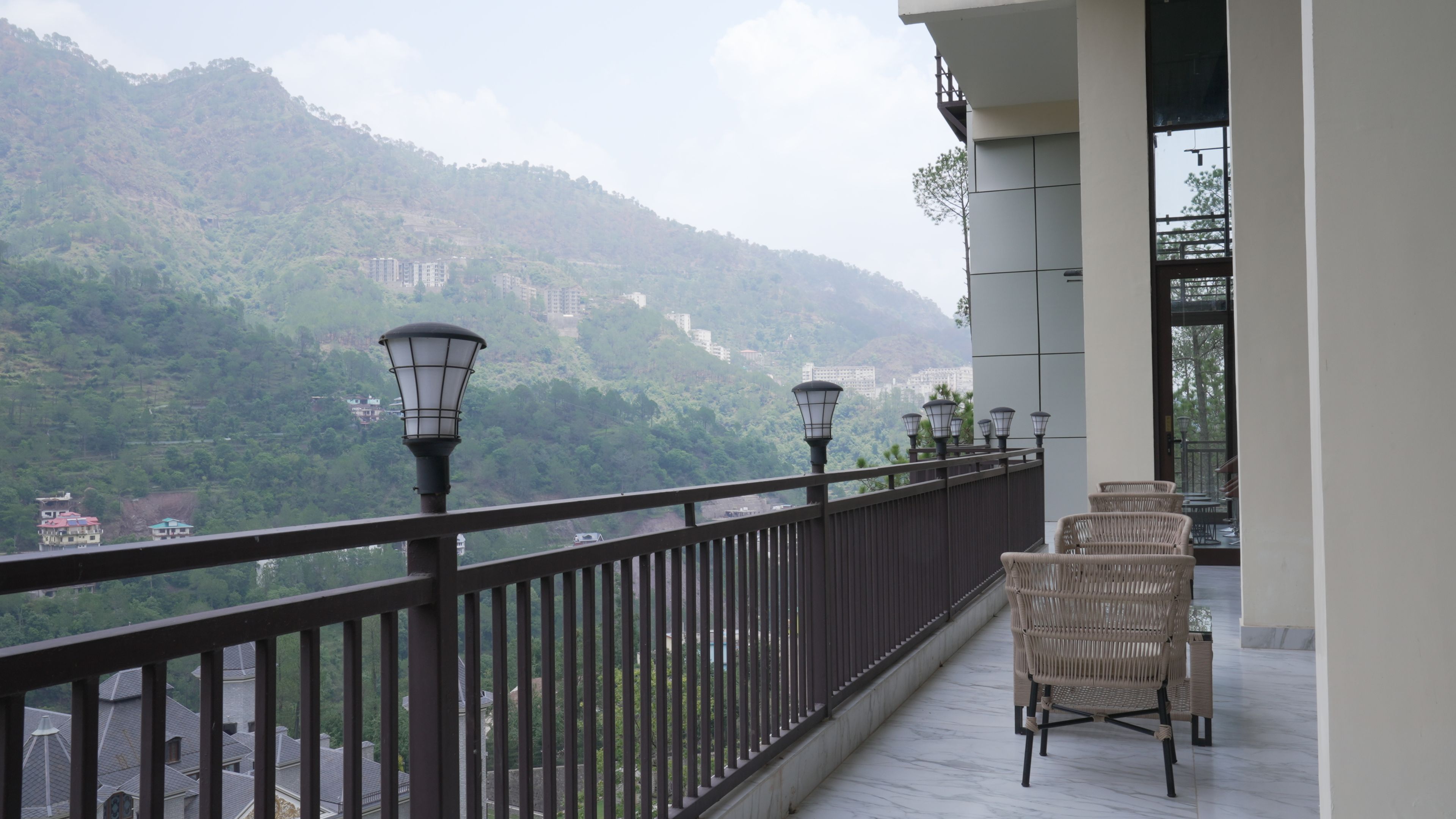 A balcony with wicker chairs and a railing overlooking a mountainous landscape.