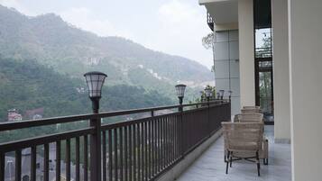 A balcony with wicker chairs and a railing overlooking a mountainous landscape.