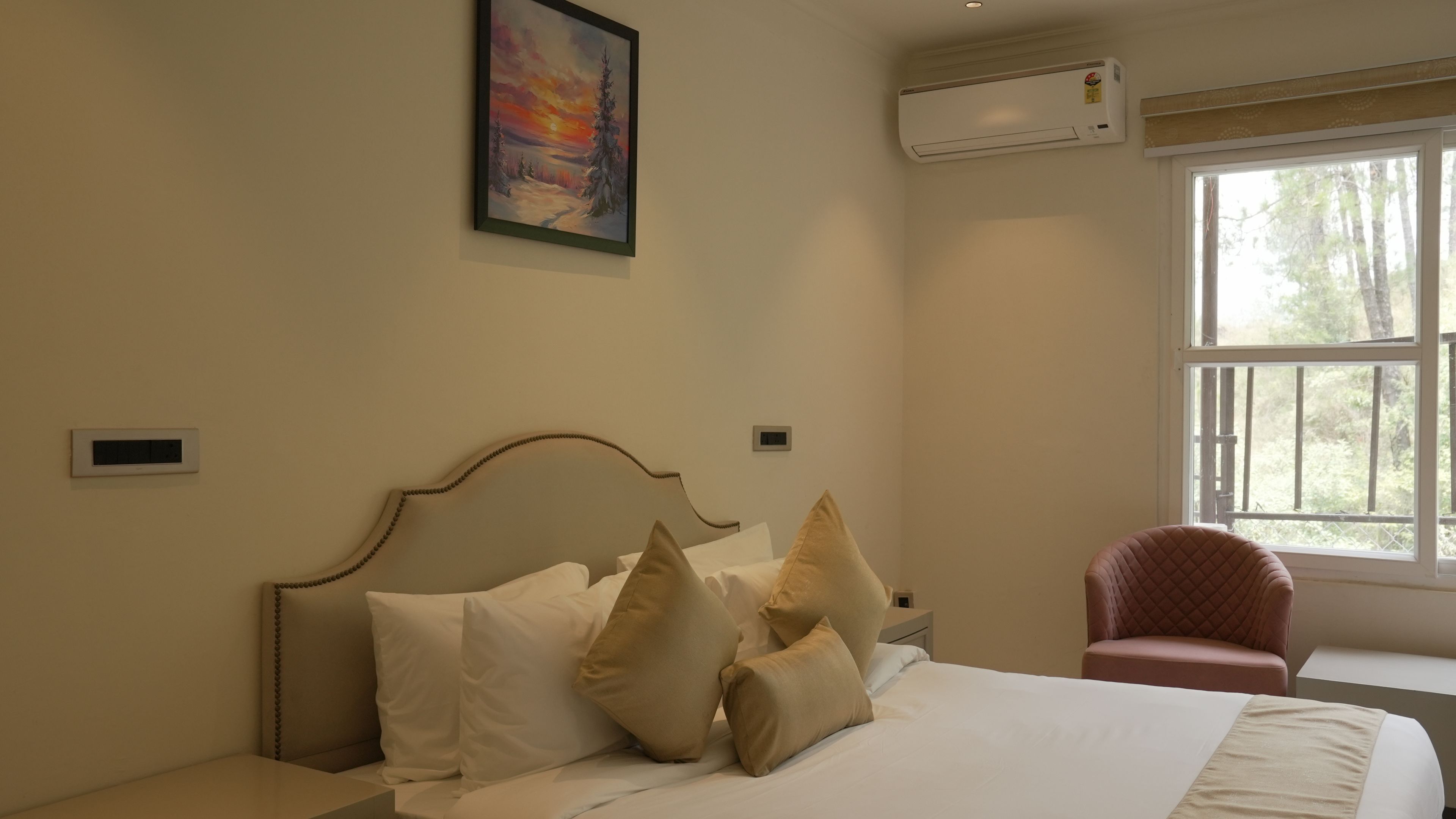 Ein Schlafzimmer mit Bett, Kissen, einem Nachttisch, einem Sessel, einem Fenster und einer Klimaanlage.