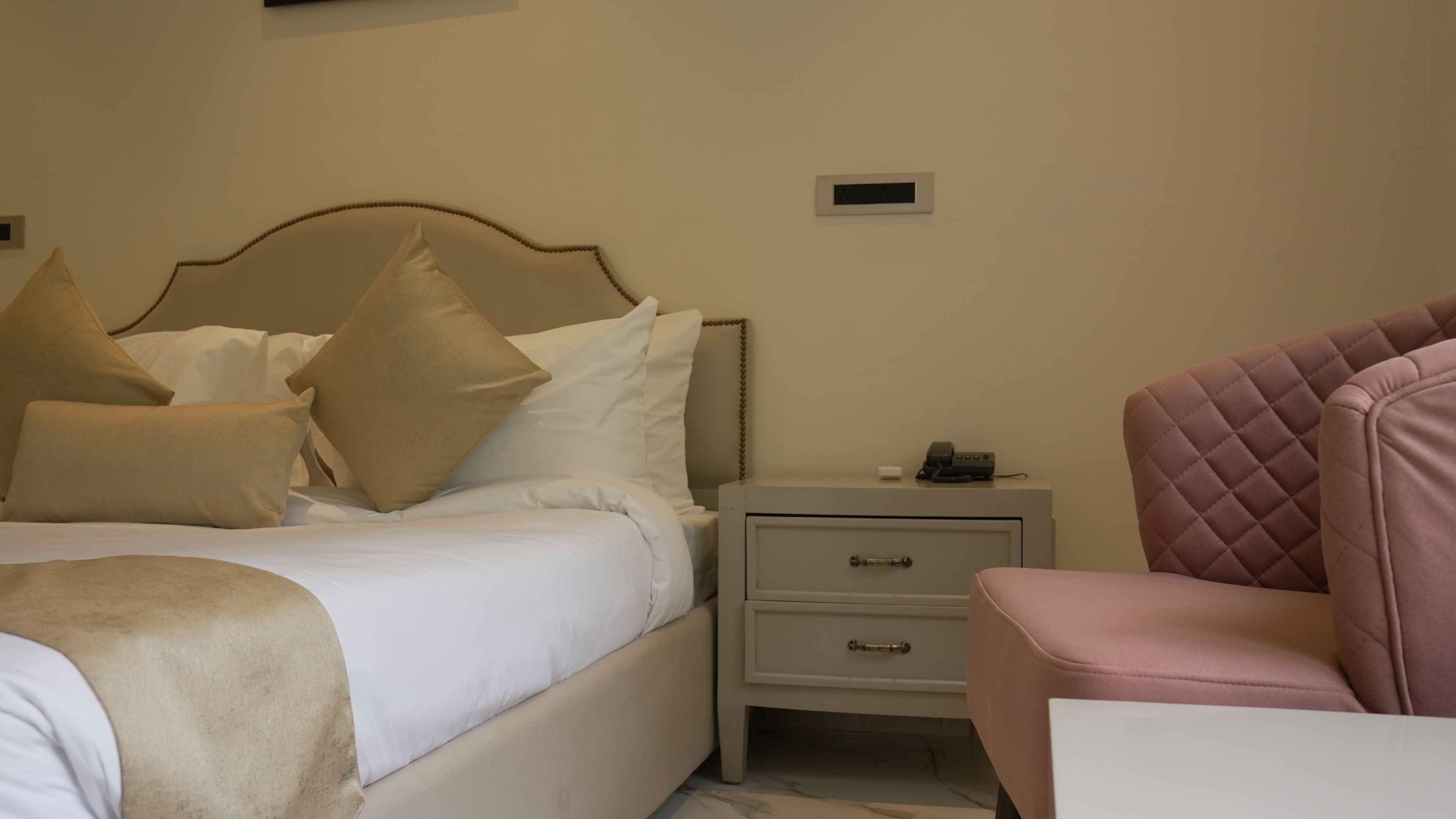 Un dormitorio con una cama, mesitas de noche, una silla y un dispositivo montado en la pared.