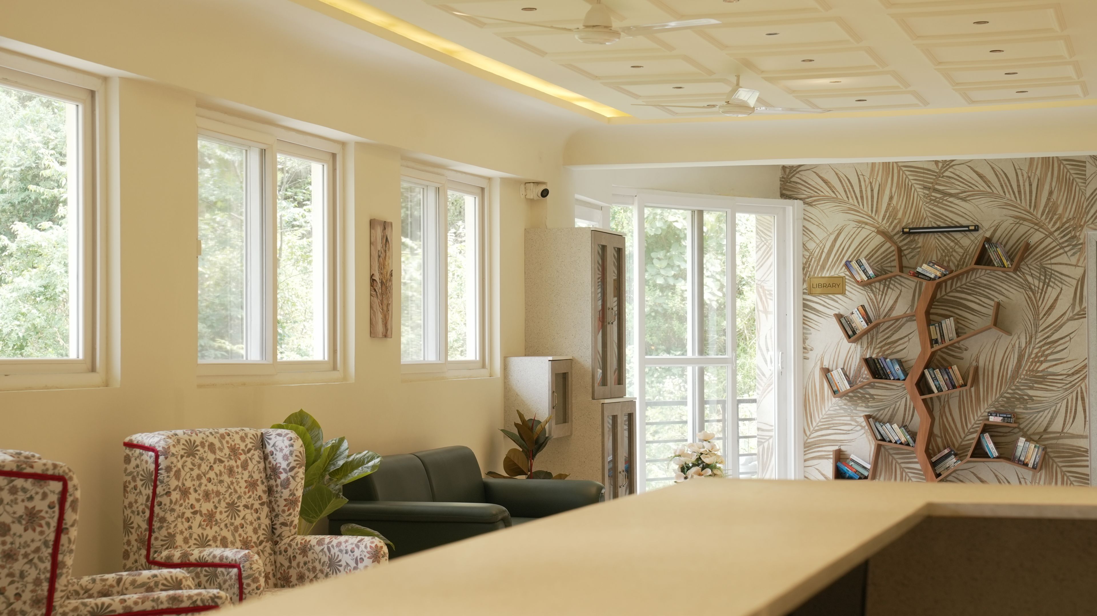 A room with large windows, a bookshelf, and a seating area.