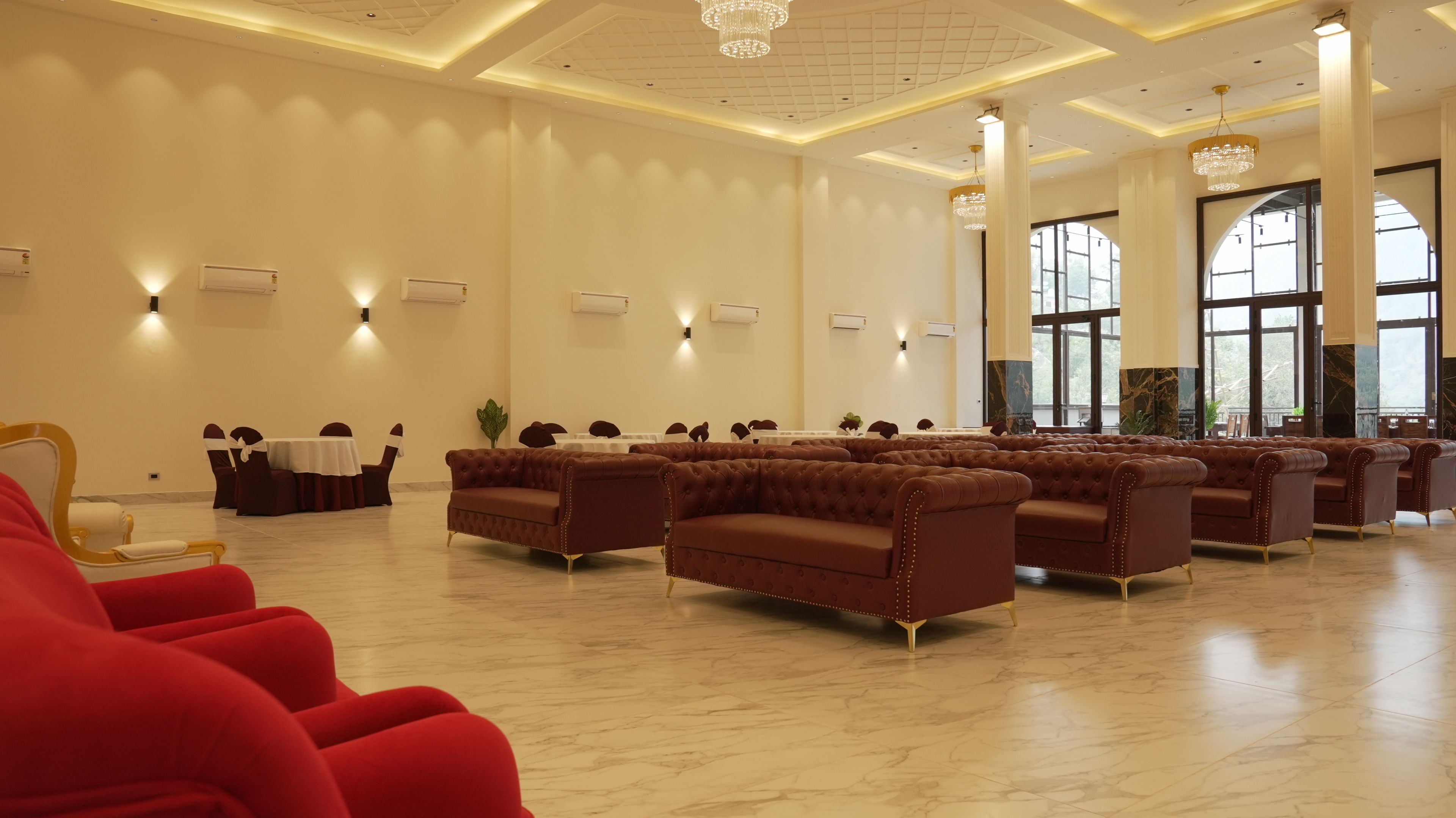 Ein geräumiger Raum mit braunen Sofas, roten Sesseln, großen Fenstern und einer Kristallleuchtre.