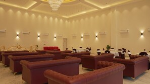A spacious room with multiple seating areas, including red cushioned sofas and a grand chair, arranged for a formal event. - Isvara (Kasauli)