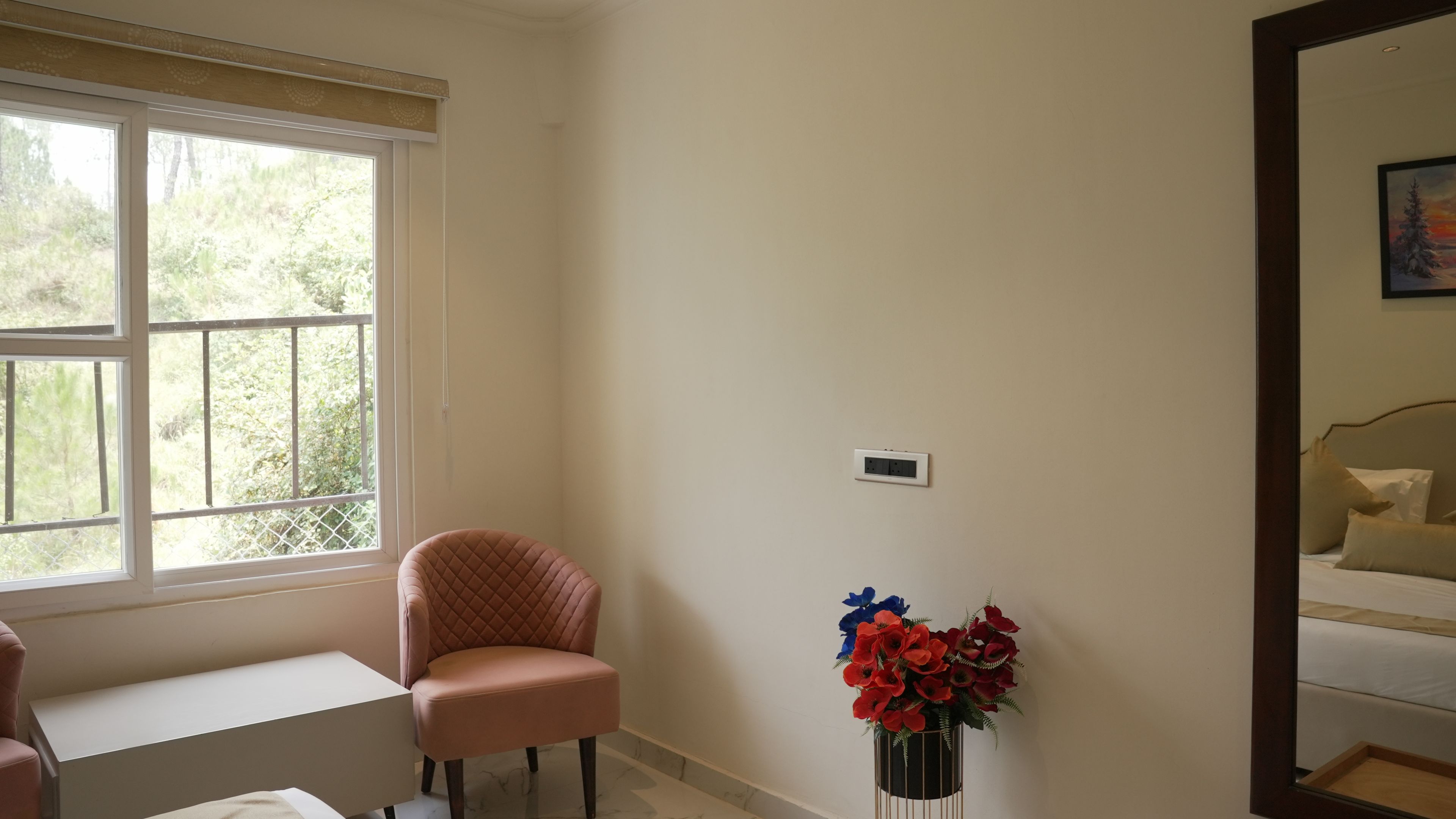 A room with a window, a chair, a bedside table, a bedside lamp, and a mirror.