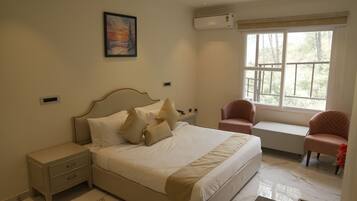 A bedroom with a bed, bedside tables, a chair, a window, and a painting on the wall.