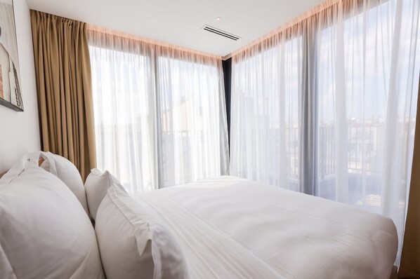 Ein Hotelzimmer mit einem großen Bett, beigen Vorhängen und Blick auf die Stadt.