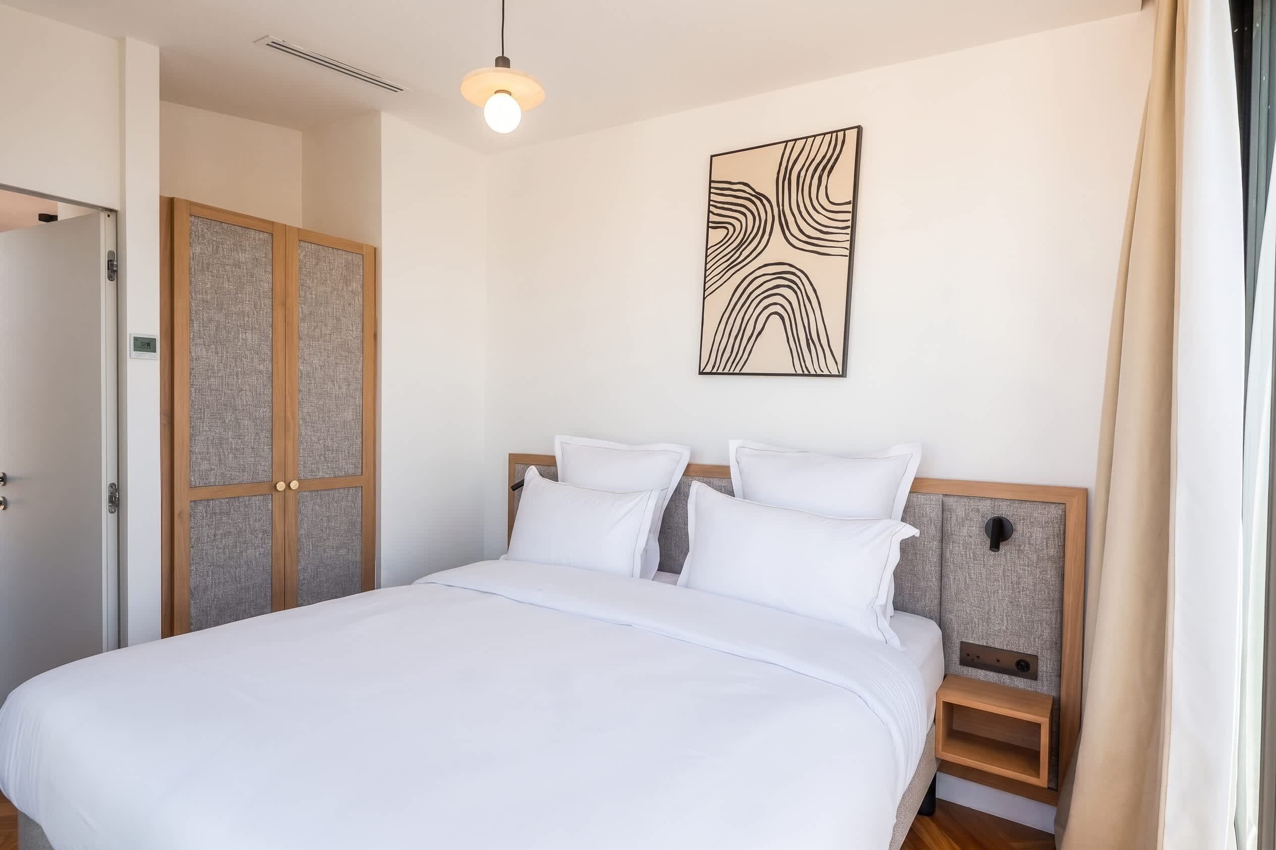 A bedroom with a bed, a nightstand, a wall-mounted artwork, and a door with a textured panel.