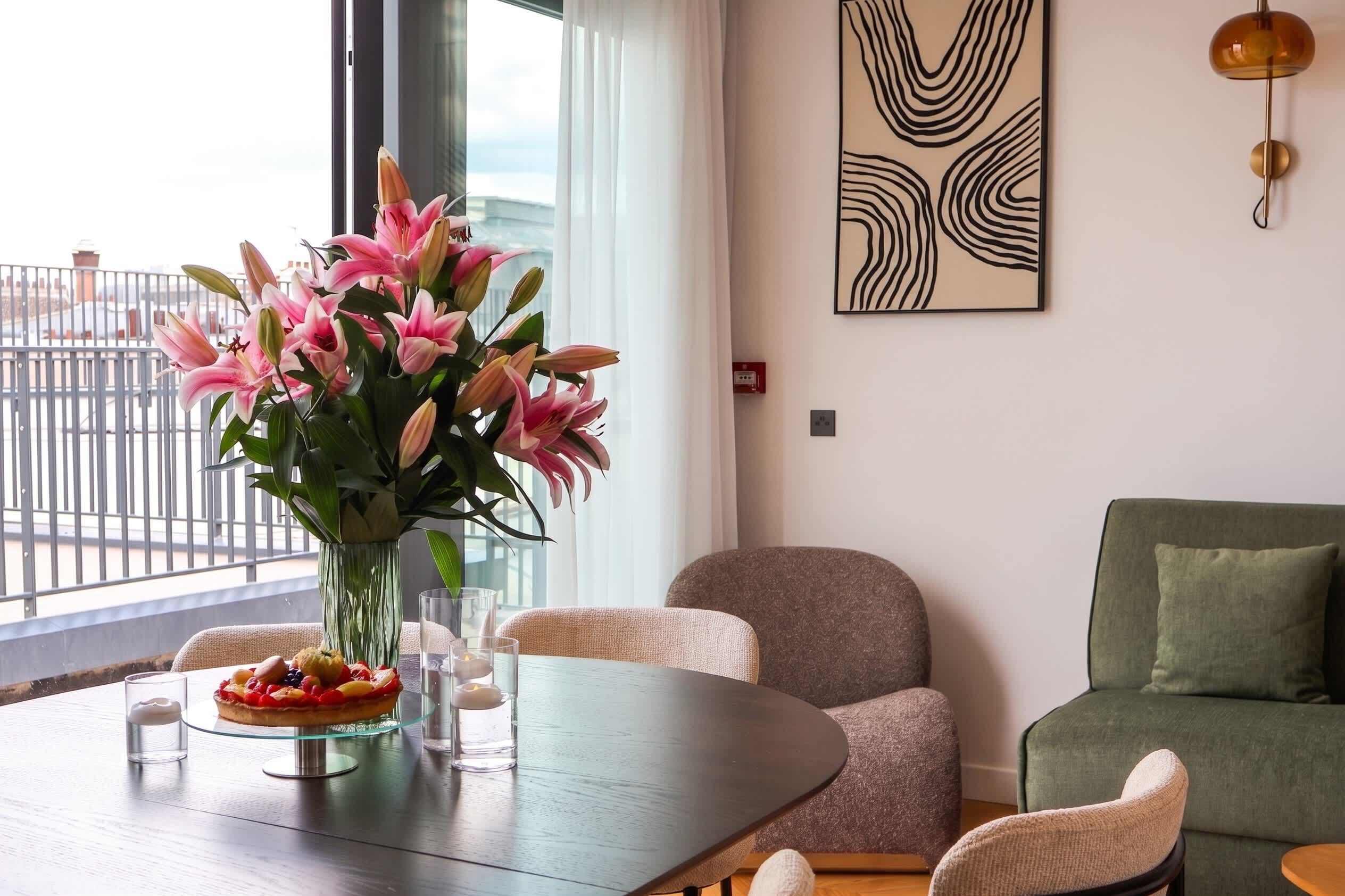 Un salon moderne avec une table à manger, des chaises, un vase de fleurs et un tableau accroché au mur.