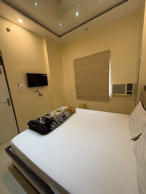 Una habitación de hotel con una cama, un televisor en la pared y un equipo de aire acondicionado.