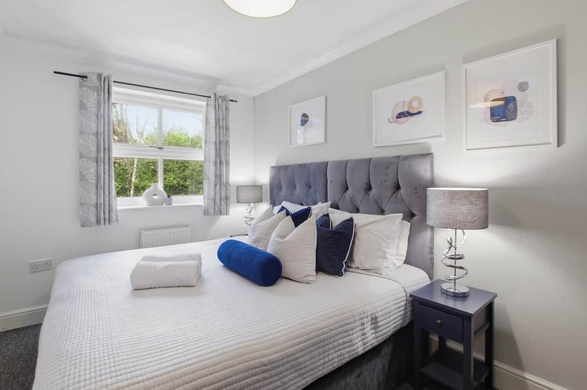 A bedroom with a large bed, a bedside table with a lamp, and a window with curtains.