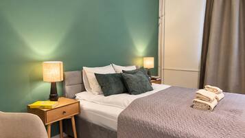 Ein Hotelzimmer mit einem Bett, Nachttischen, Lampen, einem Sessel und einem Fenster mit Vorhängen.