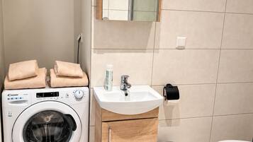 A compact bathroom with a washing machine, a sink, a mirror, and a toilet.