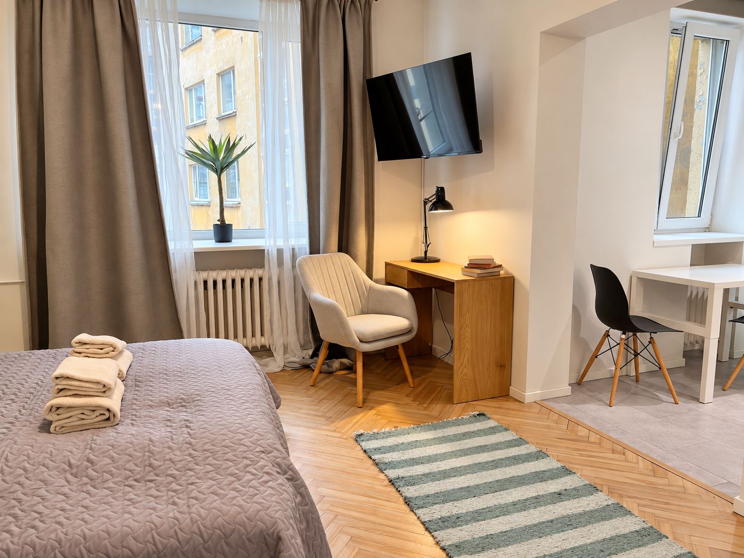 Una habitación de hotel con cama, escritorio, silla, televisor y ventana con cortinas.
