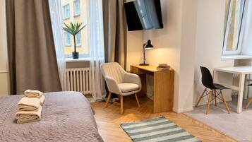 A hotel room with a bed, a desk, a chair, a TV, and a window with curtains.