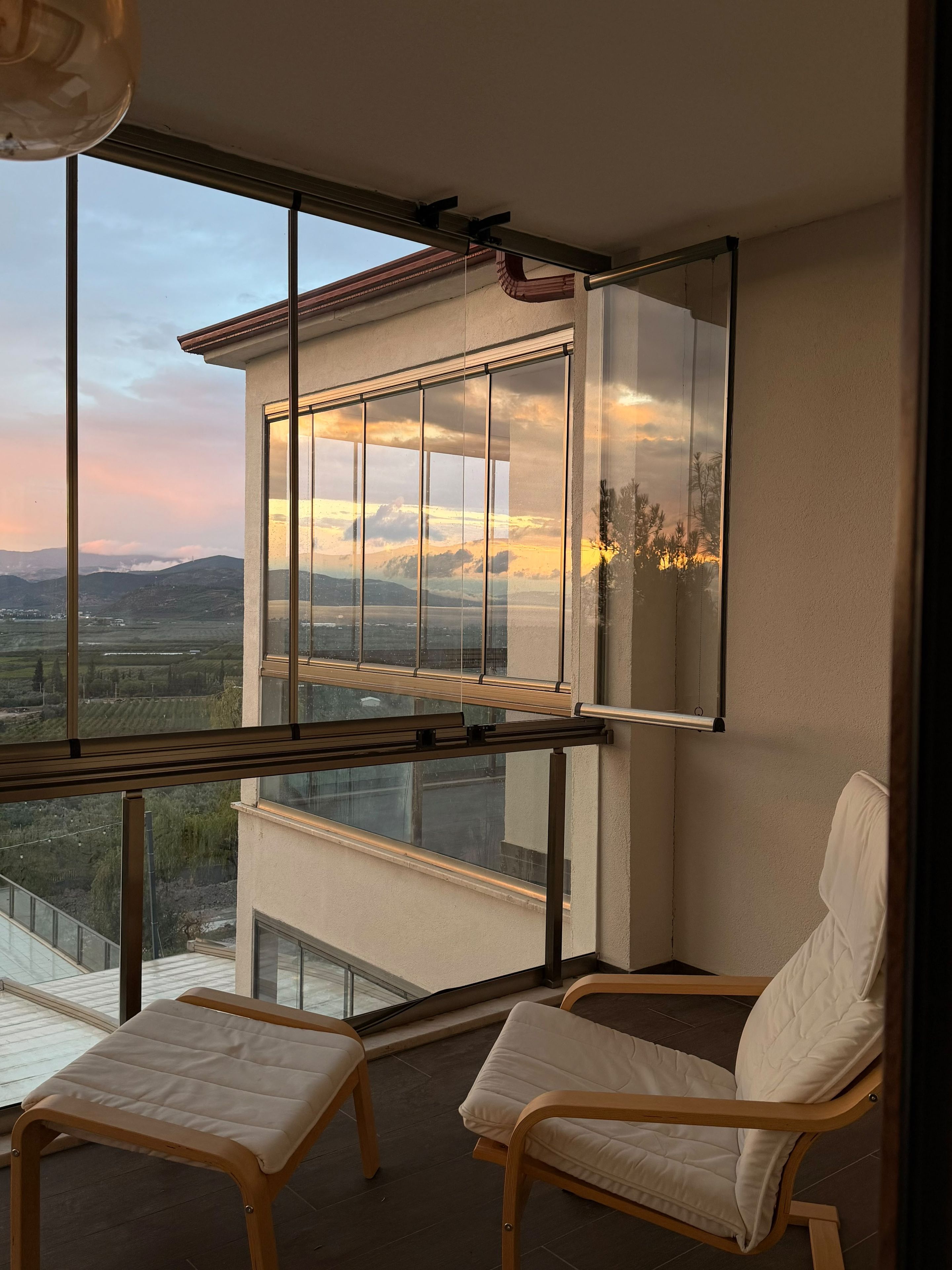 Ein Balkon mit Blick auf eine Landschaft, zwei Stühle und ein Fenster mit Himmelsblick.
