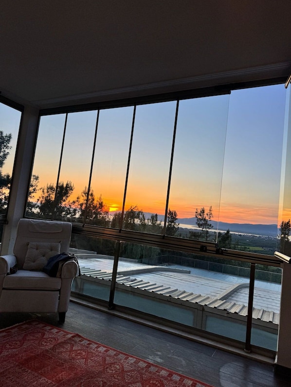 Una habitación con un gran ventanal que da a un paisaje al atardecer.