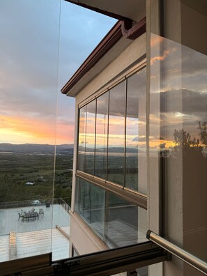 Une grande fenêtre donnant sur un paysage au coucher du soleil.