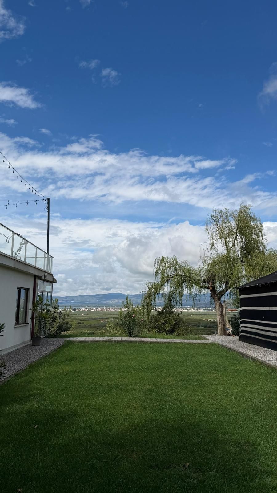 Un jardín con césped con vista a un lago y montañas, un árbol, y un edificio con balcón.