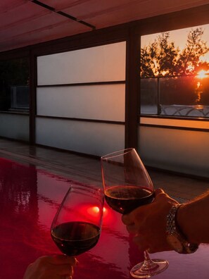Une vue sur le coucher de soleil à travers une fenêtre, avec deux verres à vin posés sur une table.