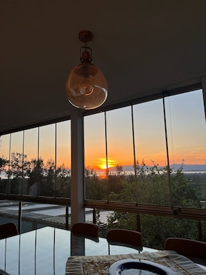 A dining area with a table and chairs, large windows, and a hanging light fixture.